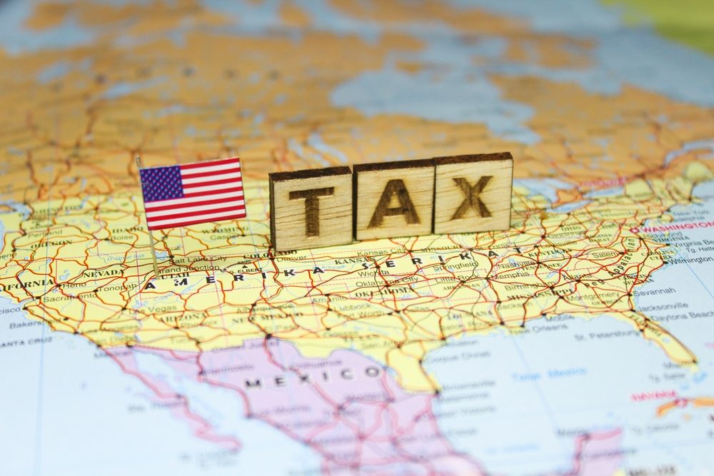 Wooden letter blocks spelling "TAX" sit beside a U.S. flag on a map of the United States, symbolizing state and local tax planning, compliance, and consulting services.