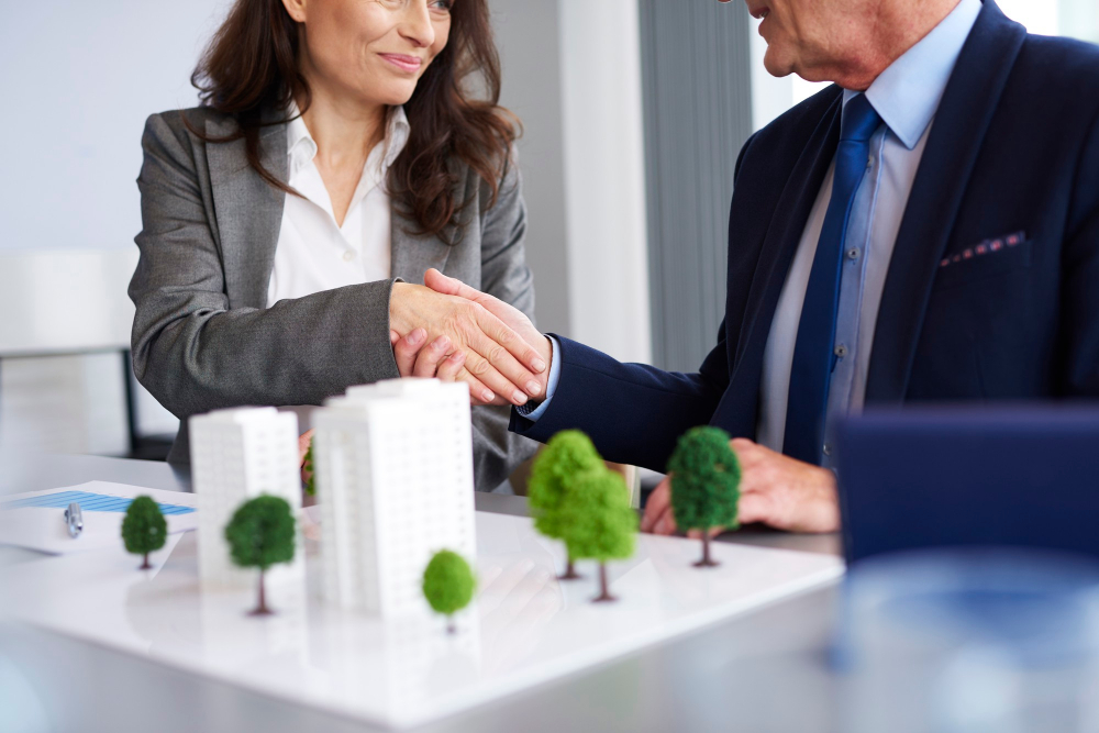 A financial professional and client shake hands after a meeting, with a property model on the table symbolizing estate planning, tax strategy, and long-term financial planning.