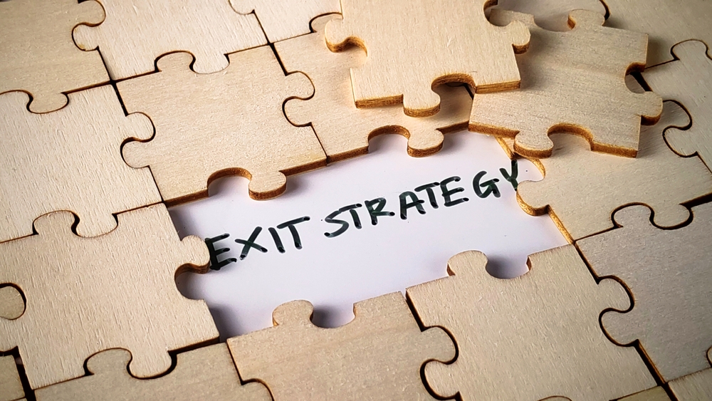 Wooden puzzle pieces reveal the words "Exit Strategy," symbolizing business succession and transition planning.